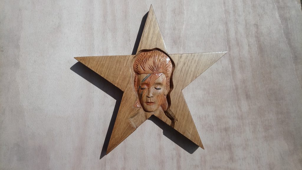 A woodcarving with tinted areas showing David Bowie as Aladdin Sane
