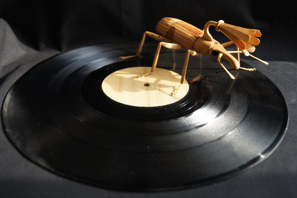 A wooden sculpture of an insect with a gramophone horn on its back, playing a record