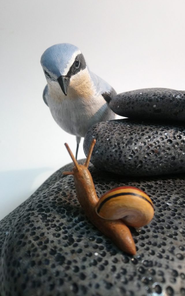 a painted woodcarving of a wheatear bird and a banded snail